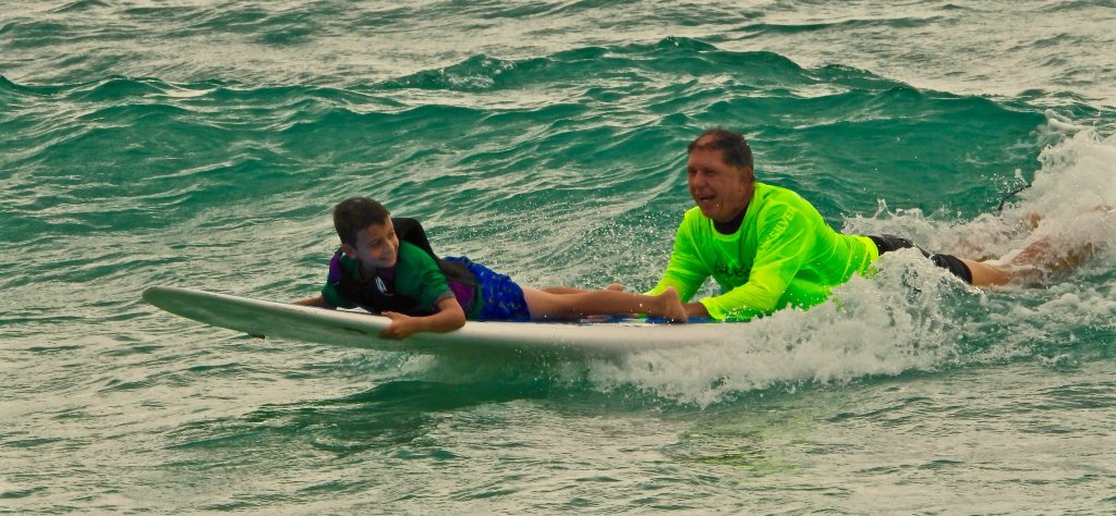 AccesSurf Instructor rides a wave with a happy participant