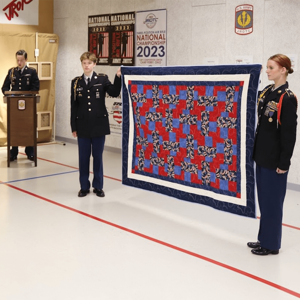 Cadet Ayat narrates the ceremony while Cadets Henry and Moseley display the Quilt of Valor.