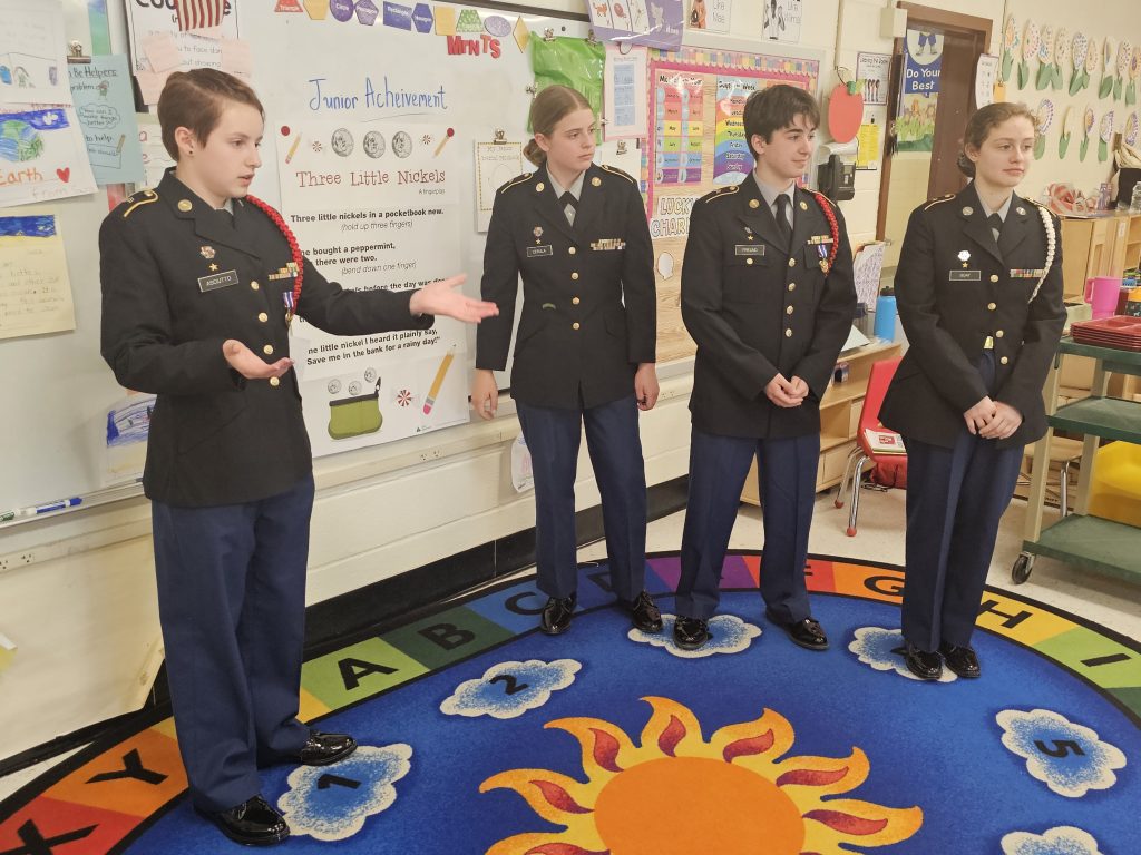 Cadets Olivia Asciutto, Alyssa Cerula, Daniel Freund and Sophie Guay present a class on saving money to the Kindergarteners