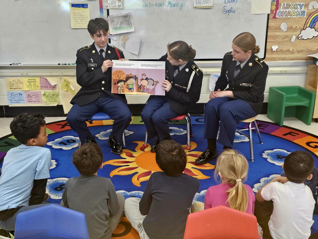 Cadets Daniel Freund, Sophie Guay and Alyssa Cerula read a story about creating a garden to the Kindergarten class.